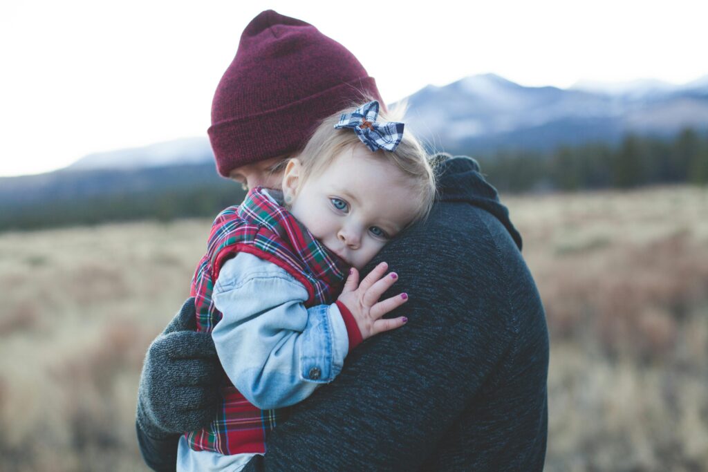 A father and child embrace outdoors with a winter mountain backdrop.